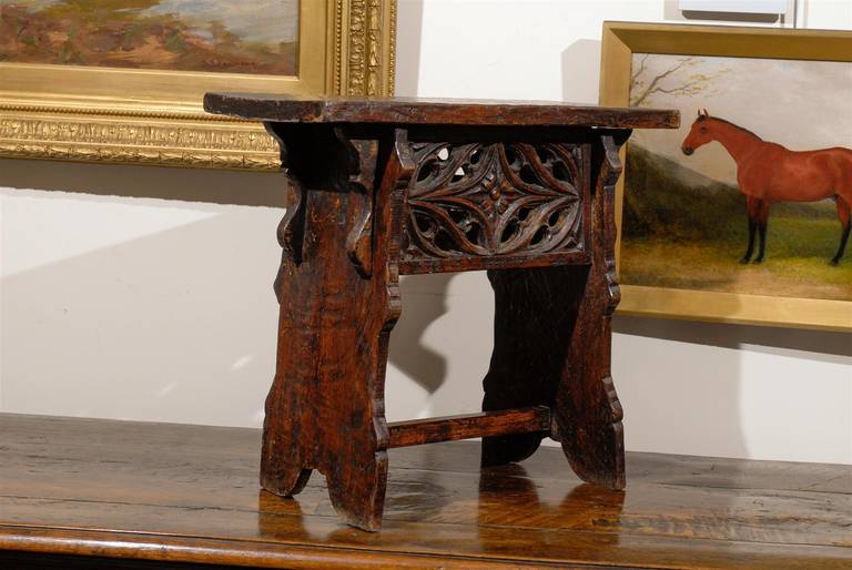 A Spanish early 20th century richly carved wooden bench or stool. This Spanish wooden bench or stool from circa 1920 features a rectangular top over a trestle base with slightly slanted sides and a cross stretcher. The focal point of this Spanish