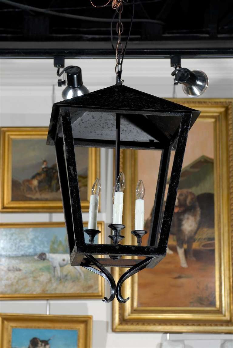 This vintage French four-light iron lantern from the mid-20th century is newly wired for the United States and ready to hang. The lights, attached to a central rod, sit in the centre of the four-sided body. The lower section is adorned with