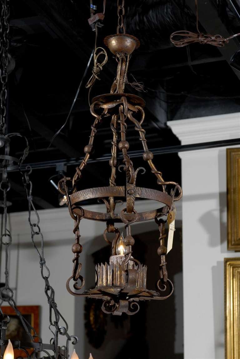 This French iron single light lantern features a serrated circular base supporting a similarly serrated and fluted bobeche receiving a single large candle. It rests on four scrolling arms connected to an upper ring with four connectors adorned with
