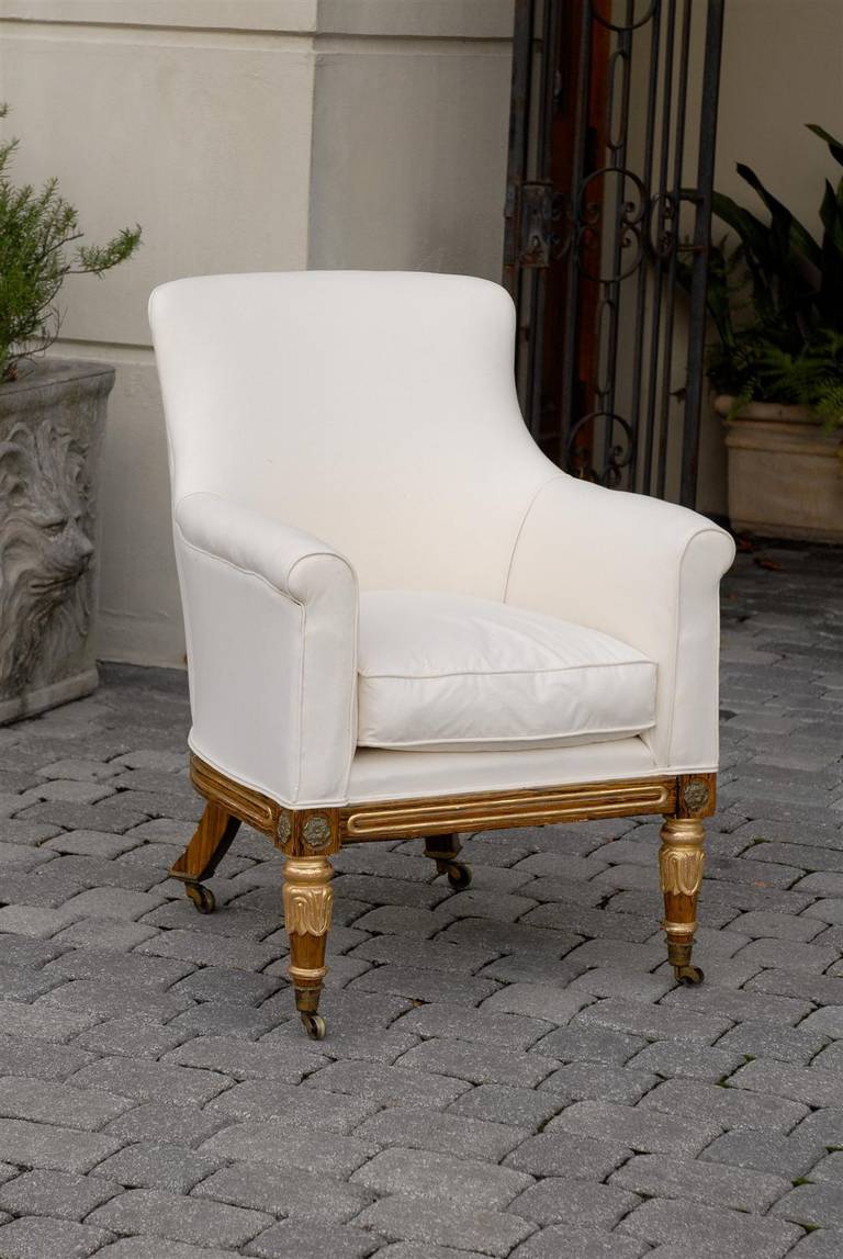 This English early 19th century period Regency armchair features a new muslin upholstered curved back, seat with cushion and arms over four exquisite short painted legs with gilded accents. The front two legs are tapered and decorated with gilded