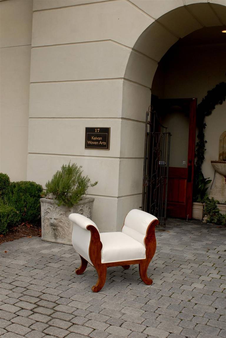 Este adorable taburete austriaco Biedermeier de nogal, de mediados del siglo XIX, presenta altos brazos acolchados que flanquean un asiento tapizado. Las sencillas líneas curvas de la parte superior se reproducen en la base, con los cuatro pies con
