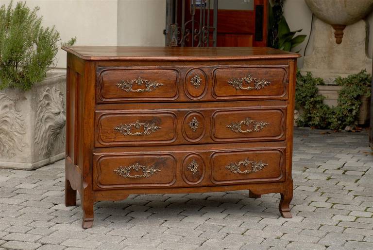 This French Louis XV style serpentine front three-drawer commode from the late 18th century features a shaped top with rounded edge and canted corners over three hand-cut dovetailed drawers, nicely revealing its old age. Each drawer is carved with
