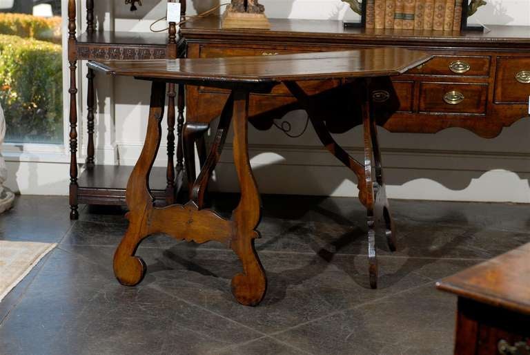A polygonal top early 19th century walnut Italian demilune console table of large size. This Italian demilune table from the early 1800 features a polygonal top over two bevelled lyre shaped trestle legs. A wooden stretcher joins the centre of the