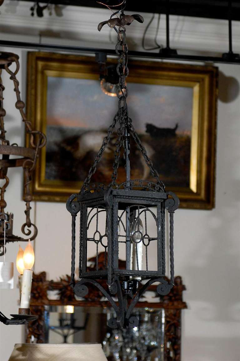 A small French iron lantern-style lantern from the mid-20th century composed of a central stem supporting three new wax sleeves enclosed in a four-sided structure adorned with openwork geometrical patterns. The structure rests on four C-shaped