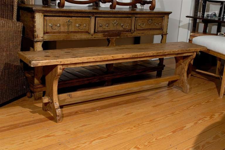 A French long pine bench with X-shaped legs from early 20th century. This French pine bench features a long rectangular seat which rests on two X-form legs connected to one another by a stretcher. The top of this bench is made from a single sturdy