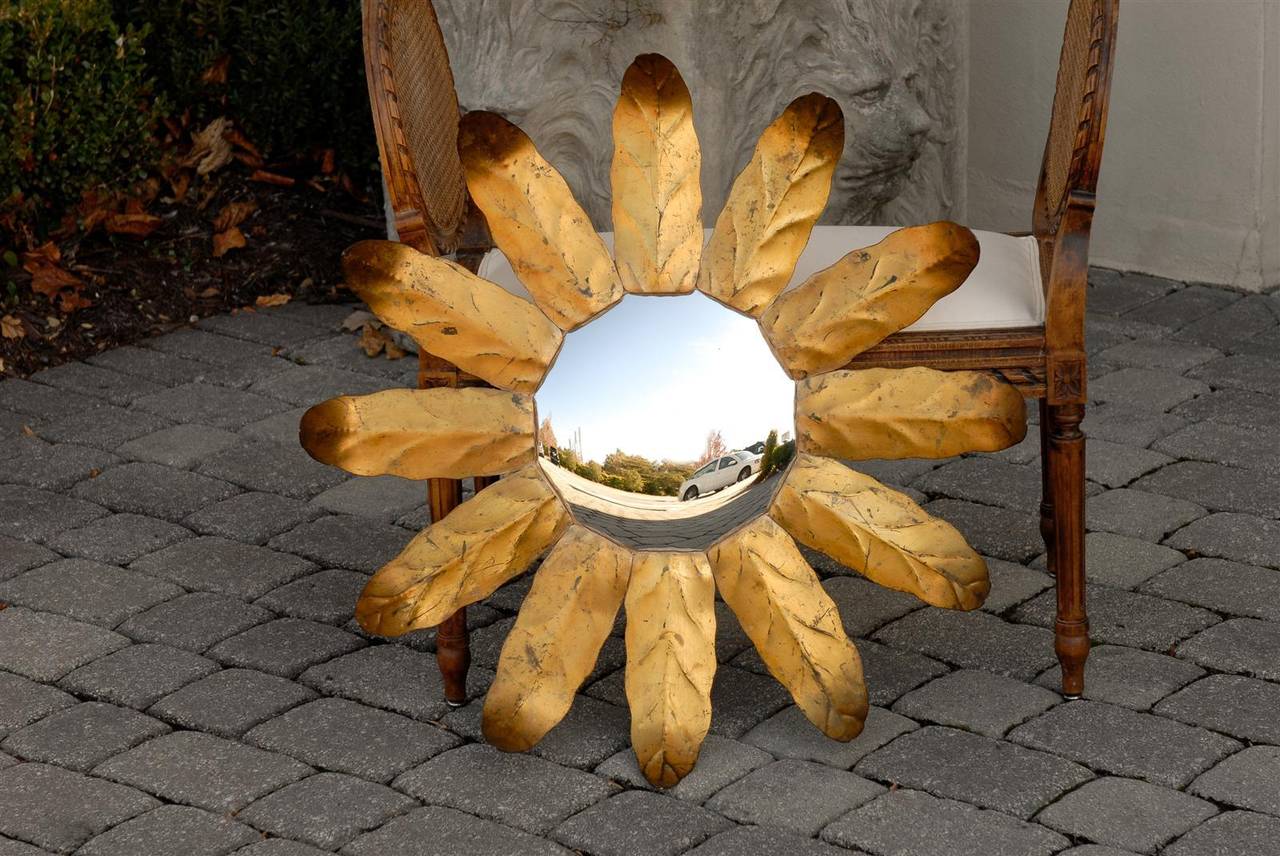 A Spanish gilt metal sunburst mirror with convex glass from the mid-20th century. This captivating Spanish gilt metal sunburst mirror crafted in the 1940s, exudes a timeless charm and artistic flair. The round mirror is encased in an unusual frame