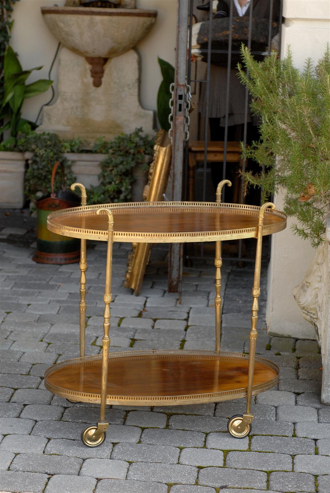 An Italian vintage oval mahogany and brass trolley from the 1950s. This Italian two-tiered tea cart features two mahogany shelves, each surrounded by a delicate pierced brass gallery. The cart is supported by four thin brass legs, with lotiform