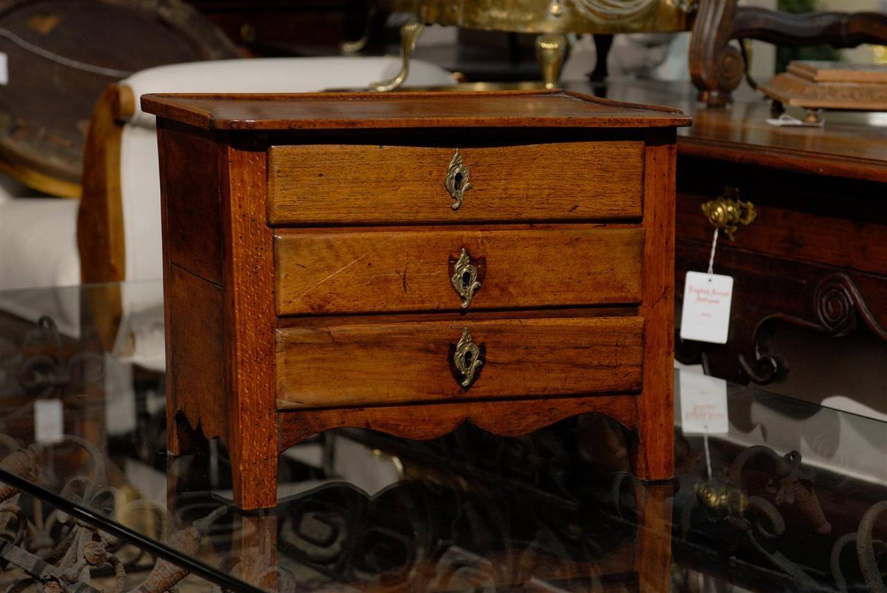 This French miniature table top commode was made of oak in the early 19th century. Using the word cute does not begin to describe this item. This miniature commode is made of three drawers with Rococo style escutcheons. The two lower drawers show