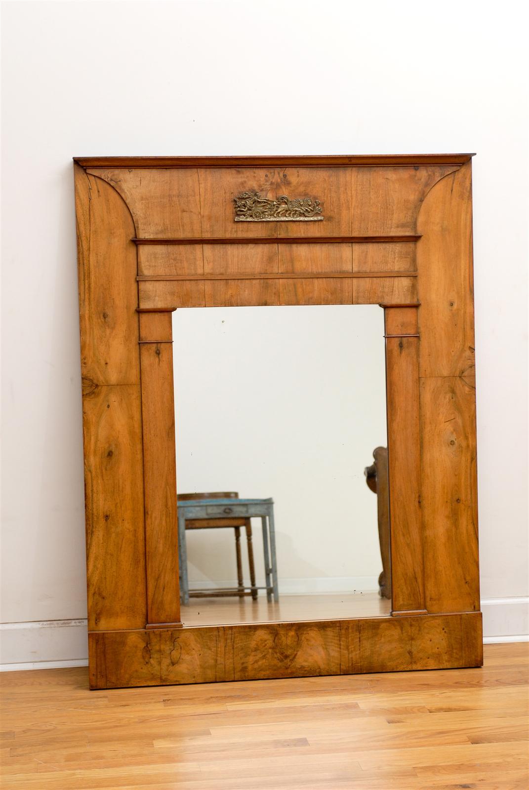 An Austrian Biedermeier tall and wide Trumeau mirror with mythological bronze mount from the mid-19th century. This Biedermeier mirror features a clean, linear wooden frame surrounding a clear glass, flanked with two Doric style pilasters. The inner