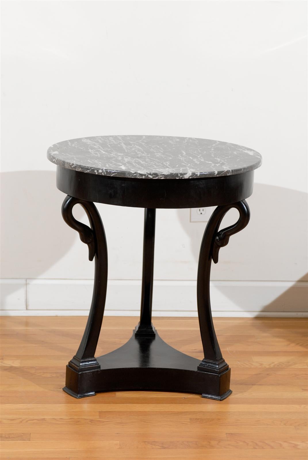 A French ebonized wood Directoire style guéridon side table with grey marble top and swan motifs from the late 19th century. This French table features a round variegated grey marble top sitting above a simple apron. The table is supported by three
