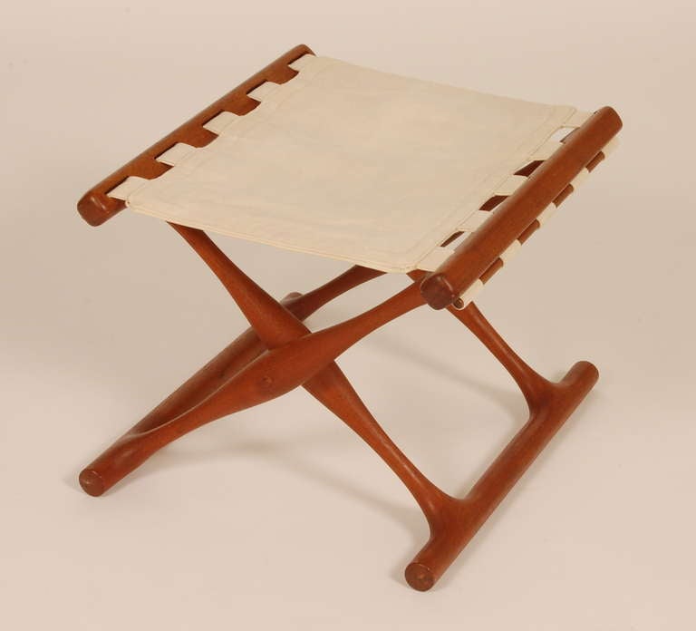 Folding teak stool by Danish designer Poul Hundevad. Canvas top and a sculptural folding base of solid teak.