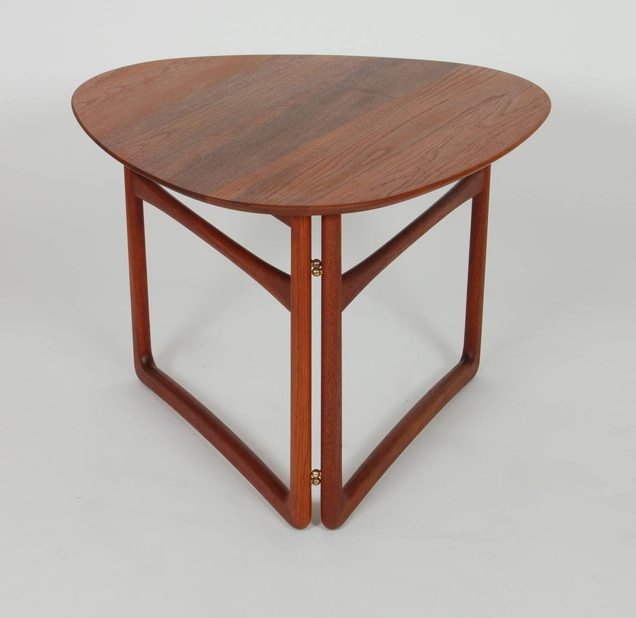 Teak folding side table designed by Peter Hvidt and Orla Molgaard-Nielsen for France and Davenkosen in 1956. Solid teak soft triangle form top that can fold down along with the legs for compact storage. The brass hinges add to the minimal design in