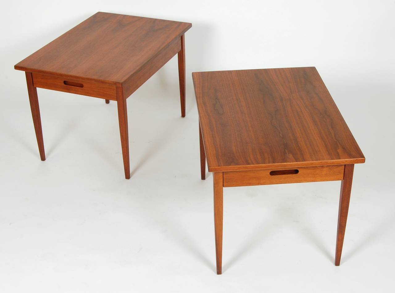Figurative walnut topped end tables with oval cut away pulls and supported by four slender legs with a slight taper. Having a very clean and minimal form with an outstanding level of construction. Restored with an oil and wax finish.