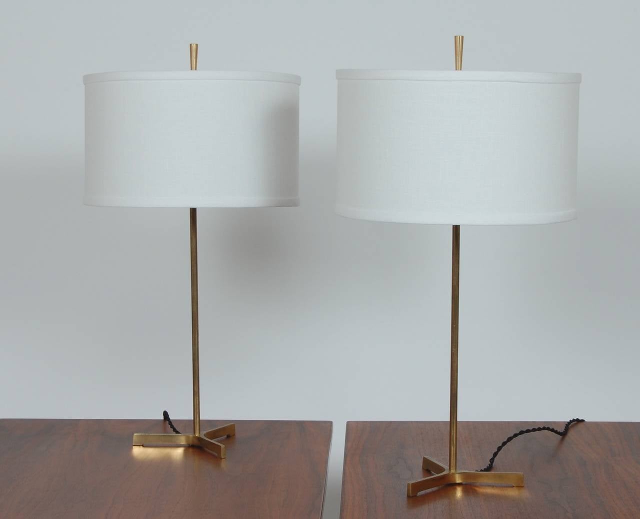 Pair of slender brass table lamps with tripod bases and linen covered drum shades with top diffusers. These lamps have been rewired and have new shades.