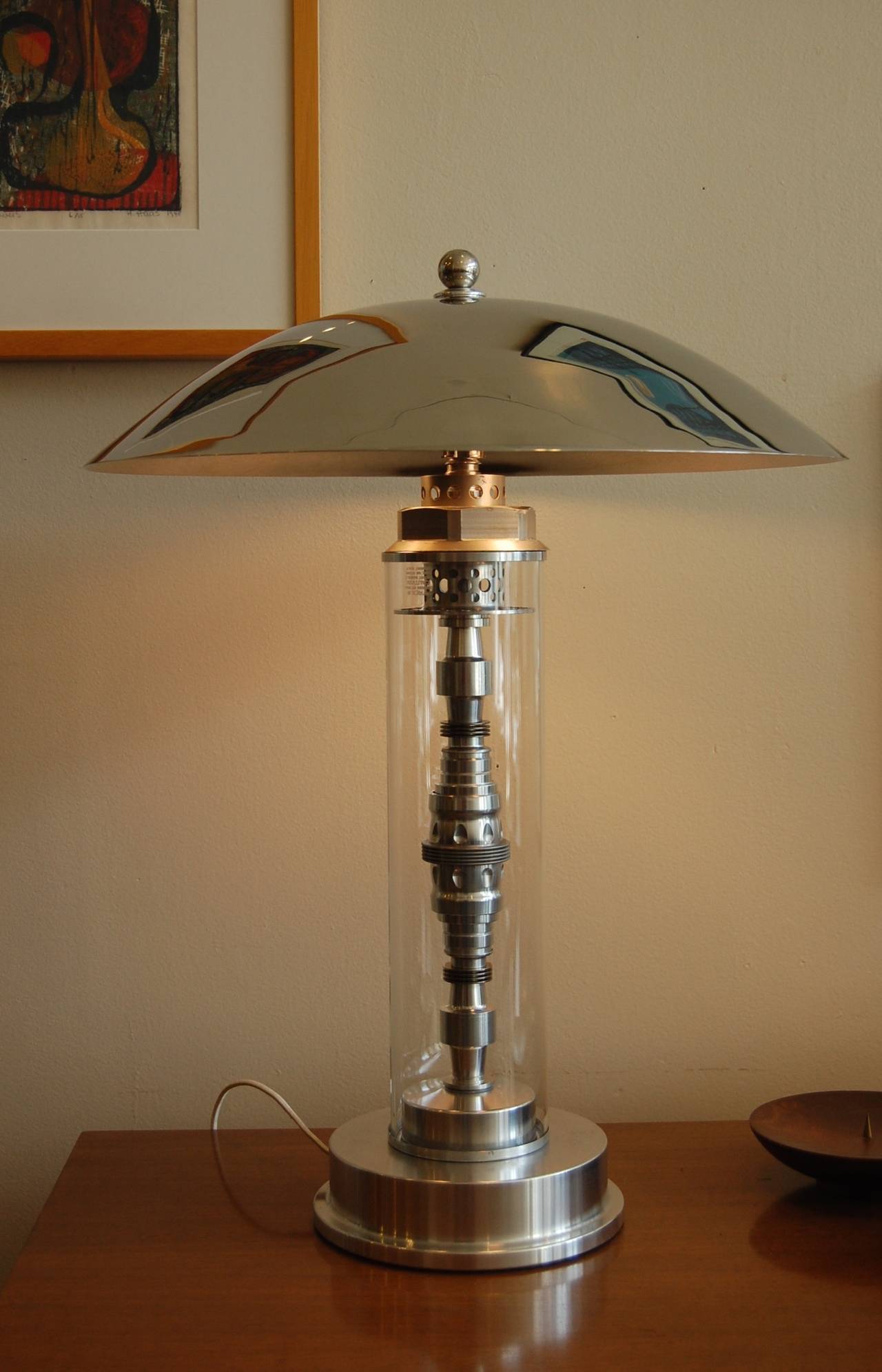 Created in the 1980s from found Industrial parts, such as a 1950s jet engine injector and a Pyrex glass cylinder is this Machine Age inspired table lamp. The shade is a heavy chrome saucer, a wonderful example of vintage assemblage in lighting.