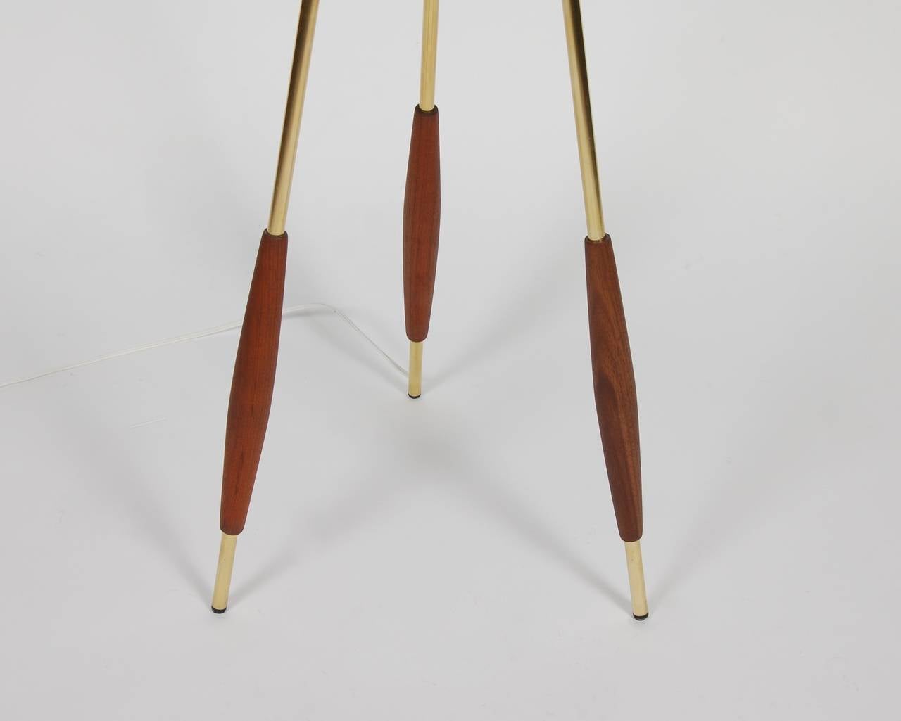 Tripod floor lamp designed by Gerald Thurston for Lightolier, hand polished brass with turned walnut accents at the base of the legs. The shade was custom-made for the lamp and still retains the original metal top diffuser. Newly rewired, the lamp