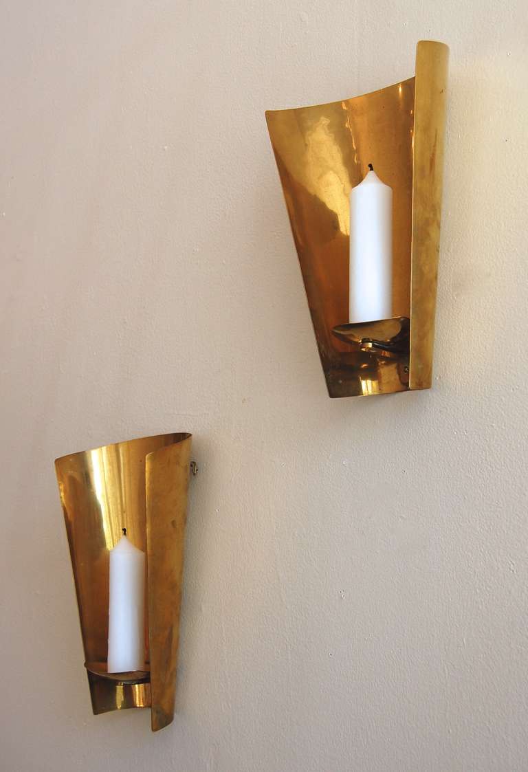 Pair of brass candle sconces with a graduated tapered curved form.