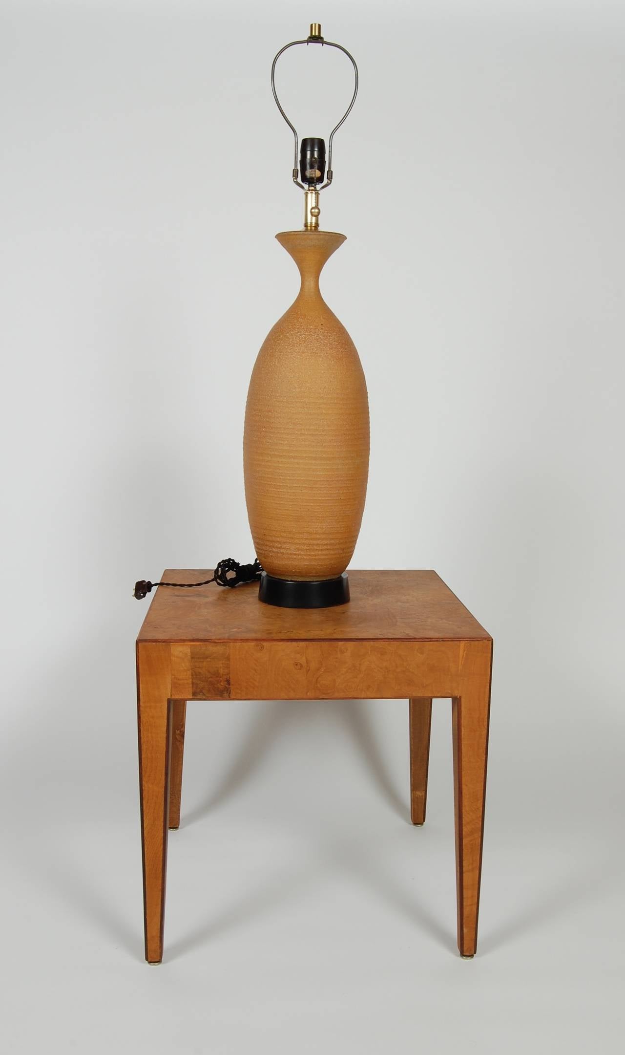 Tall and sculptural ceramic studio lamp by Bob Kinzie for his company Affiliated Craftsmen of California. Earthenware clay body with concentric grooved rings along its sides. Soft hues to the clay and resting on a black lacquered base, newly rewired.