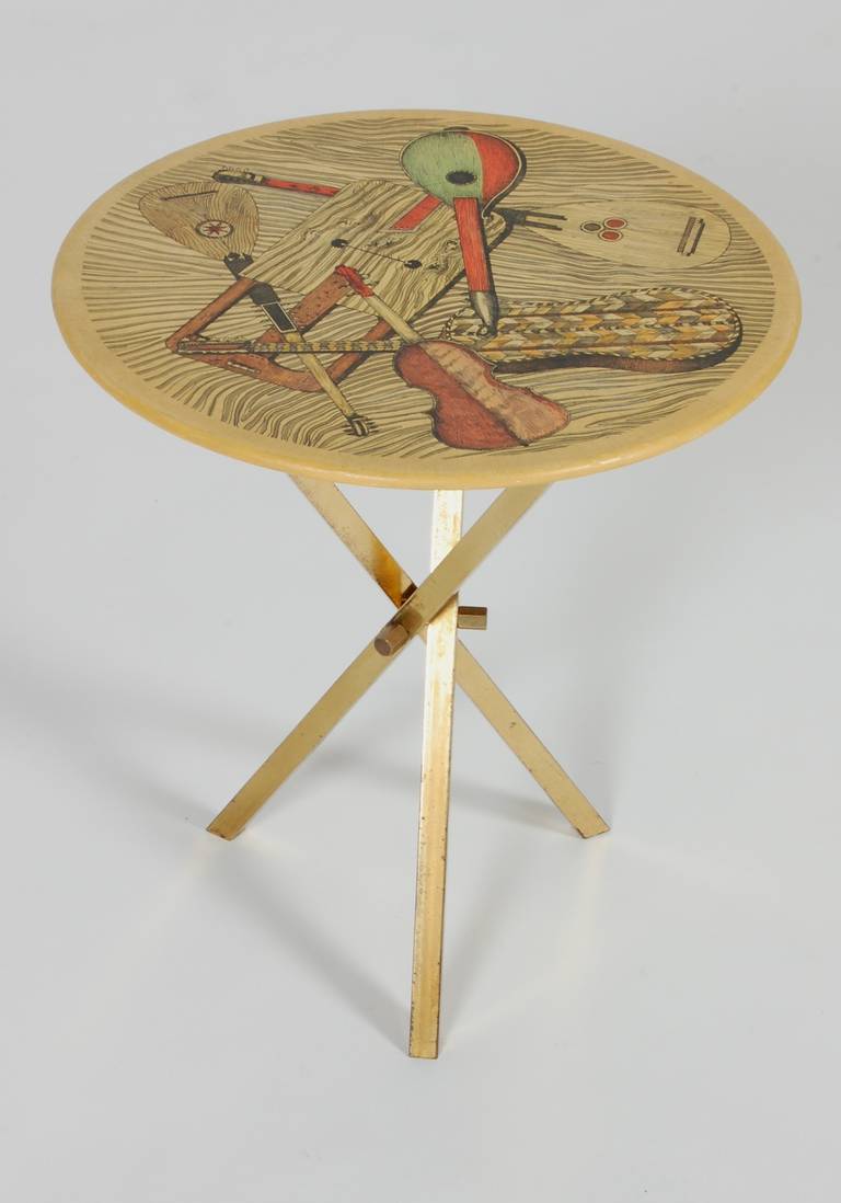A petite side table designed by Piero Fornasetti, the screened table top's motif is of musical instruments of the Middle Ages, the base is a folding square tubed brass tripod. Nice patina to the base and tabletop.