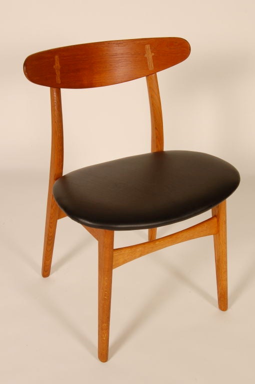 Three Hans Wegner CH-30 dining chairs, upholstered in black leather.