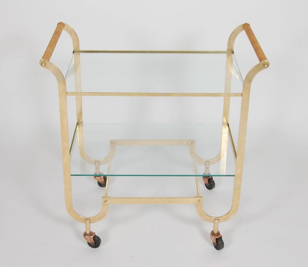 Fluid lines brass bar cart with cane handles and two glass shelves.