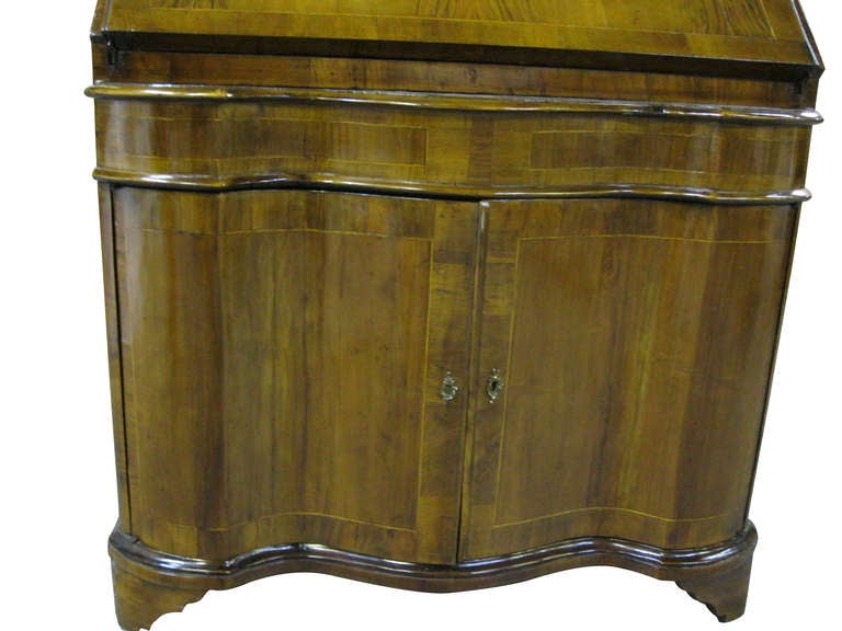Venetian walnut secretary bookcase, broken arched pediment with mirrored cartouche above double domed mirrored doors, double serpentine base. Italian circa 1940. The interior now fitted as a bar.
