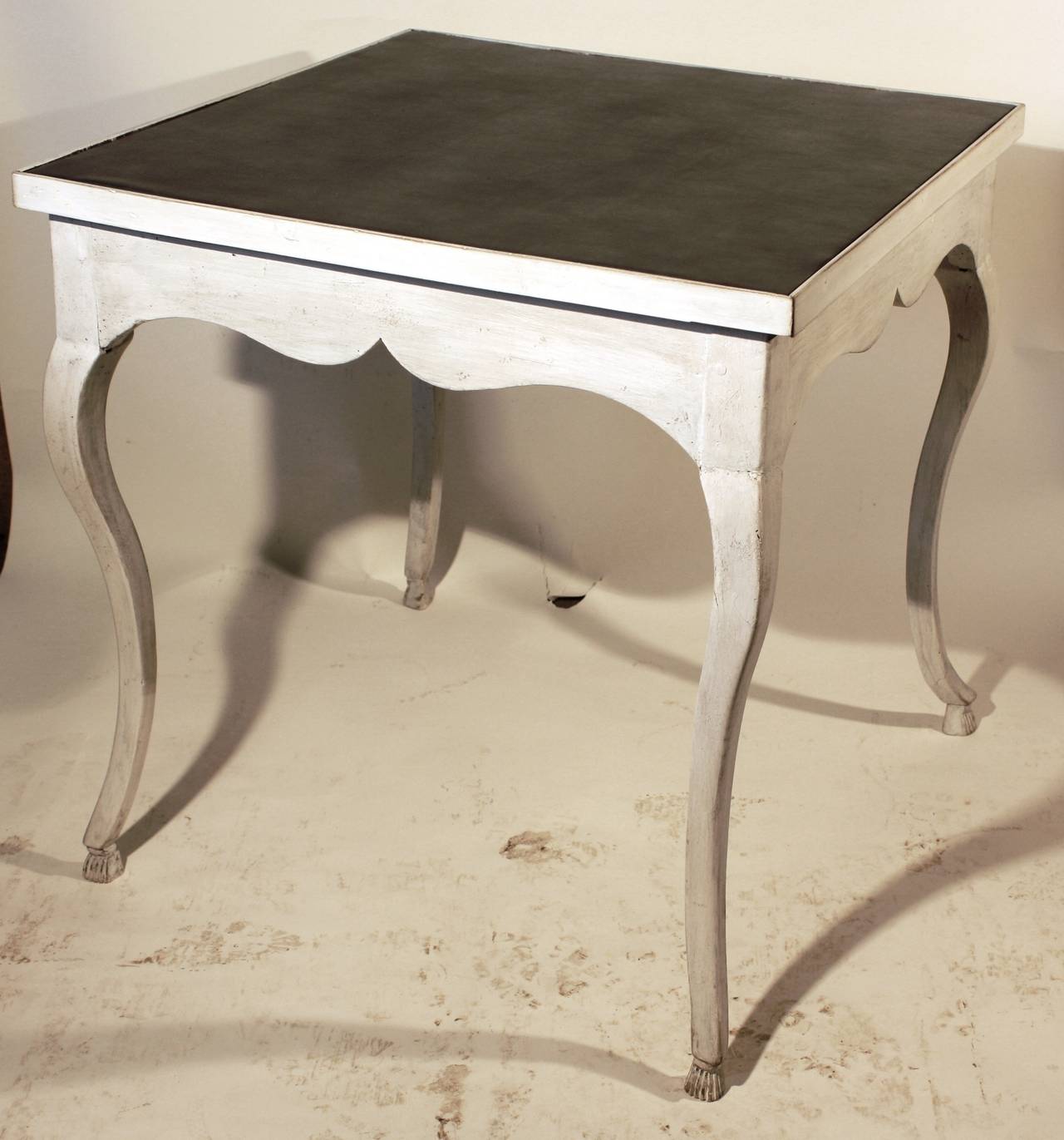 A 18th century Provincial French, Louis XV card table with grey leather top, cabriole legs with carved feet and a scalloped apron, circa 1770, in a white and grey painted finish.