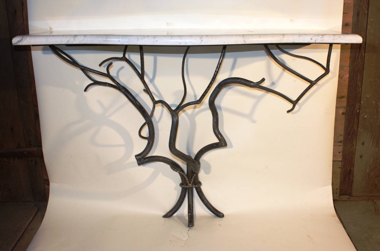A studio-made wrought iron console table in the manner of Jean-Michel Frank, the base in the form of branches with a gilt ribbon binding them and a serpentine grey or white marble top, late 20th century, unsigned.