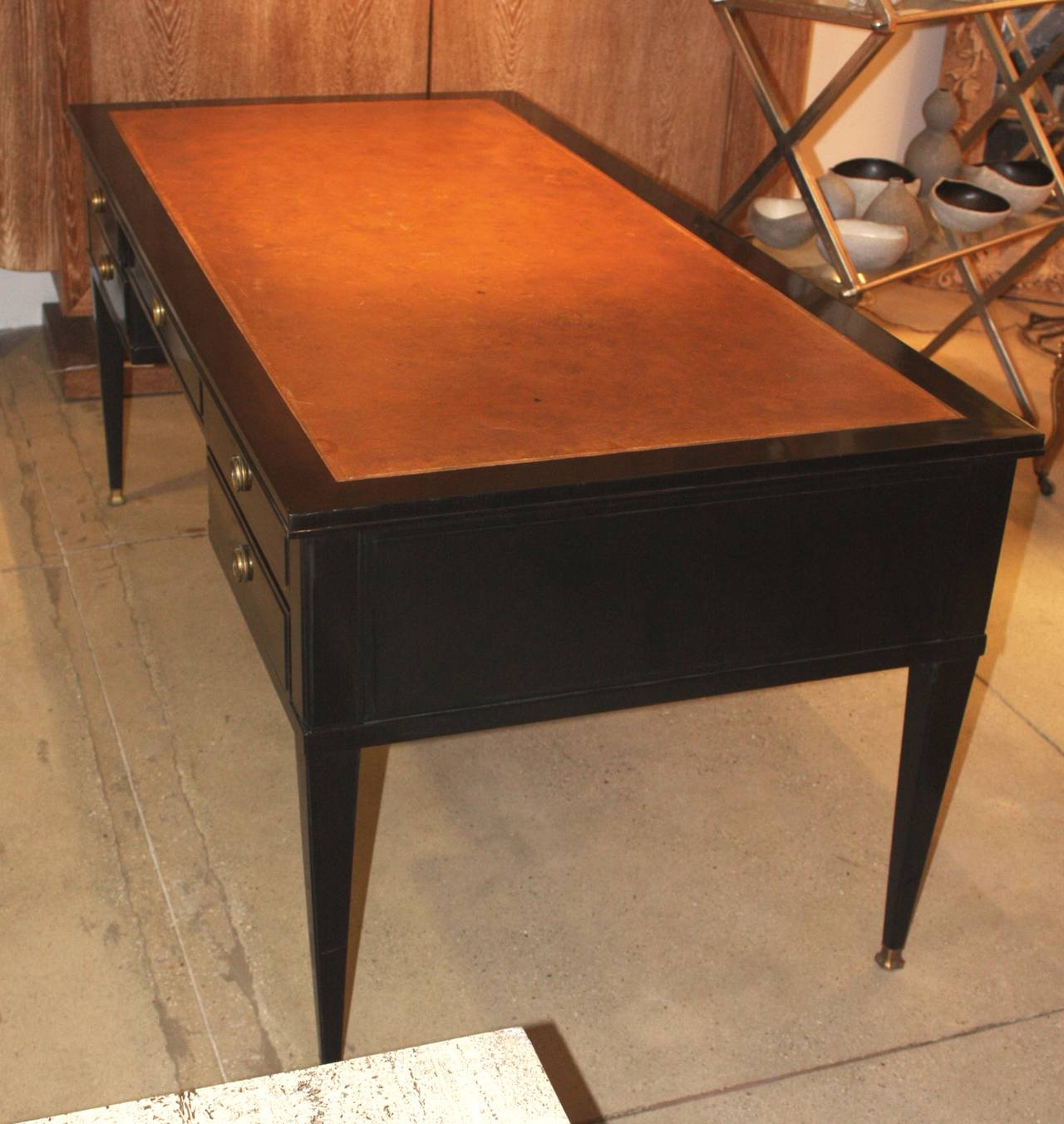 A chic 1940s Louis XVI style bureau plat in black lacquer with inset light brown tooled leather top and brass drawer pulls and sabots. The desk is by Nordiska Kompaniet and is signed in the center drawer. It has five drawers on one side and two