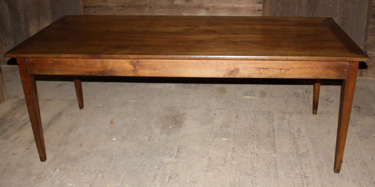 An early 19th century French cherrywood farm table with simple tapered legs, a plain apron and a pull-out cutting board on one end.