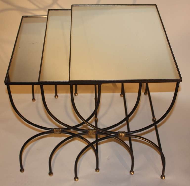 A set of 3 iron and brass nesting tables (table de gigogne) by Jean Royere, French mid 1950's, with inset mirror tops, dated on underside 
