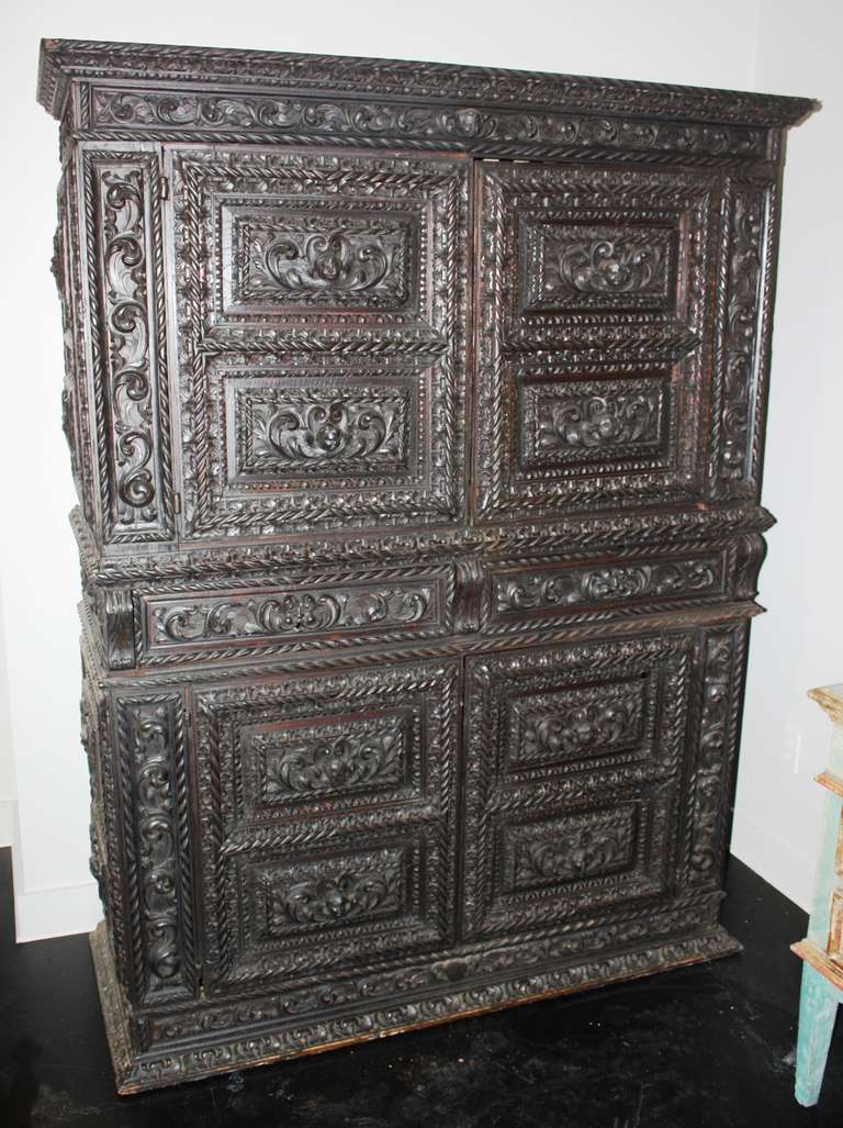 A Baroque 2-part German "Kas" in ebonized oak, circa 1780, abundantly carved with cherubs, faces, leaves, garlands etc. the upper half with 2 carved cabinet doors over a lower half with 2 drawers over a pair of doors.  