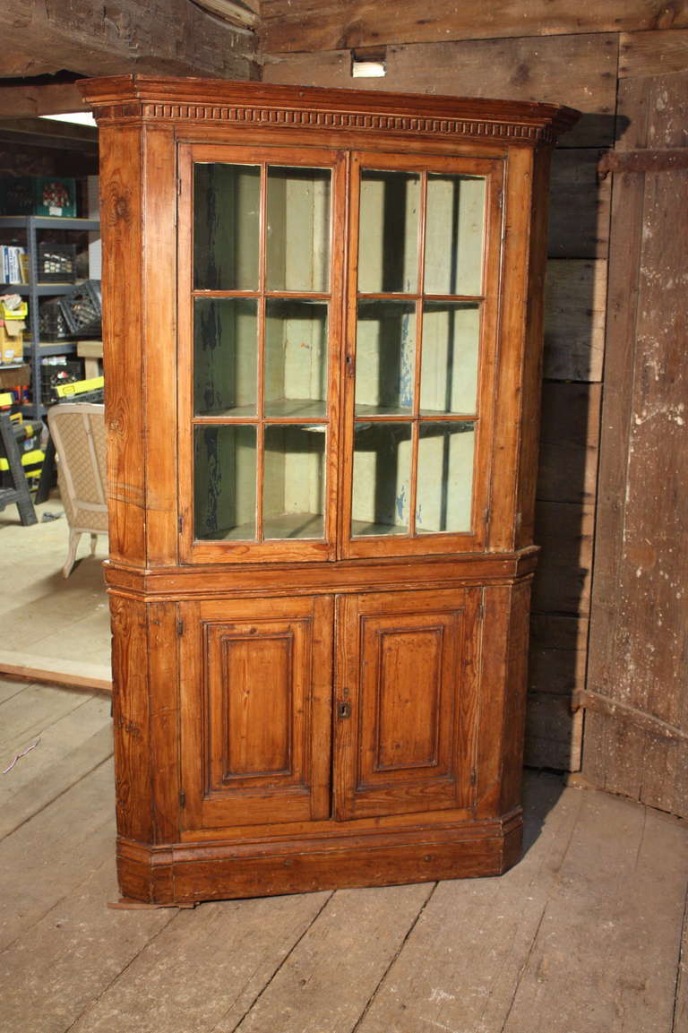 A charming 18th century pine 2-part corner cabinet, circa 1790, Pennsylvania, with glazed upper doors retaining the original wavy glass, and paneled lower doors, both cabinets with old green over blue painted finishes.