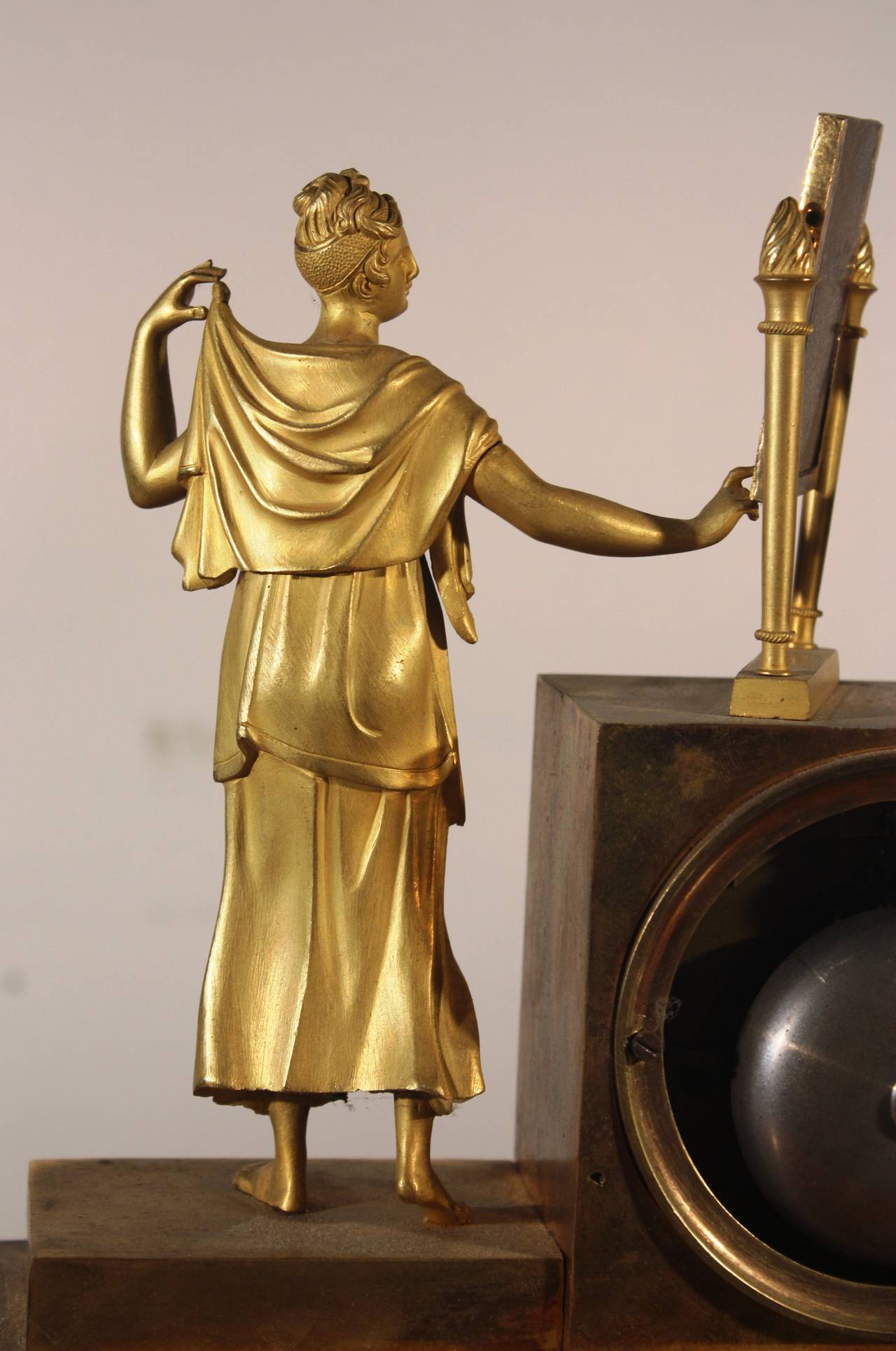 A charming French figural mantel clock, circa 1800 in gilt bronze in the form of a classically dressed woman standing before a dressing mirror. Clock chimes on the hour and is in good working order.