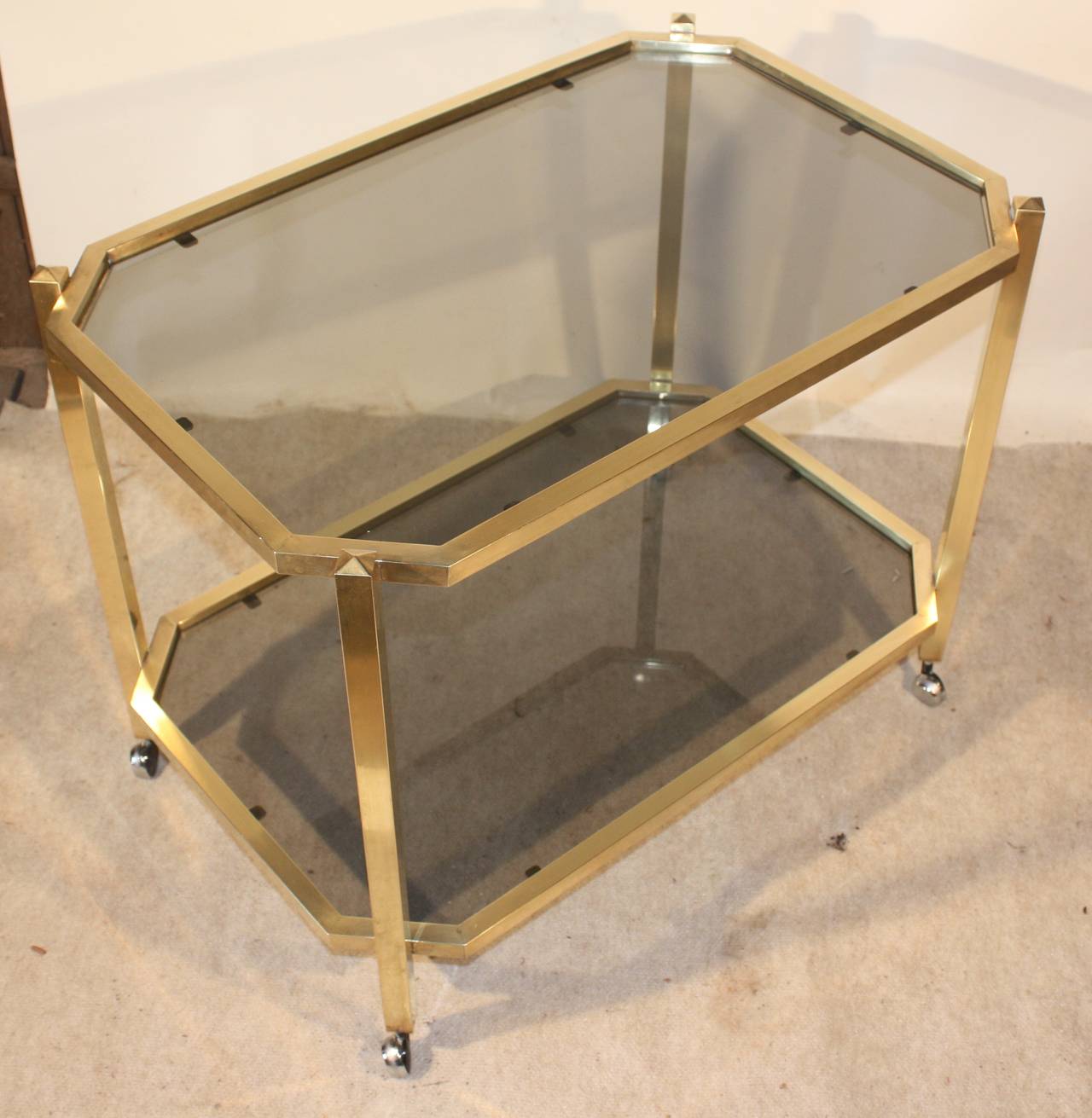 A modernist mid-century brass and smoked glass drinks cart, circa 1960, French, with chrome casters.