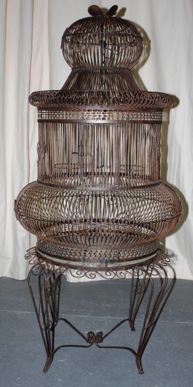 A decorative birdcage in patinated steel, circa 1940, with a separate circular base.  The top of the cage has a hook to hang it with and the base can be used as a table by inserting a glass or stone top.