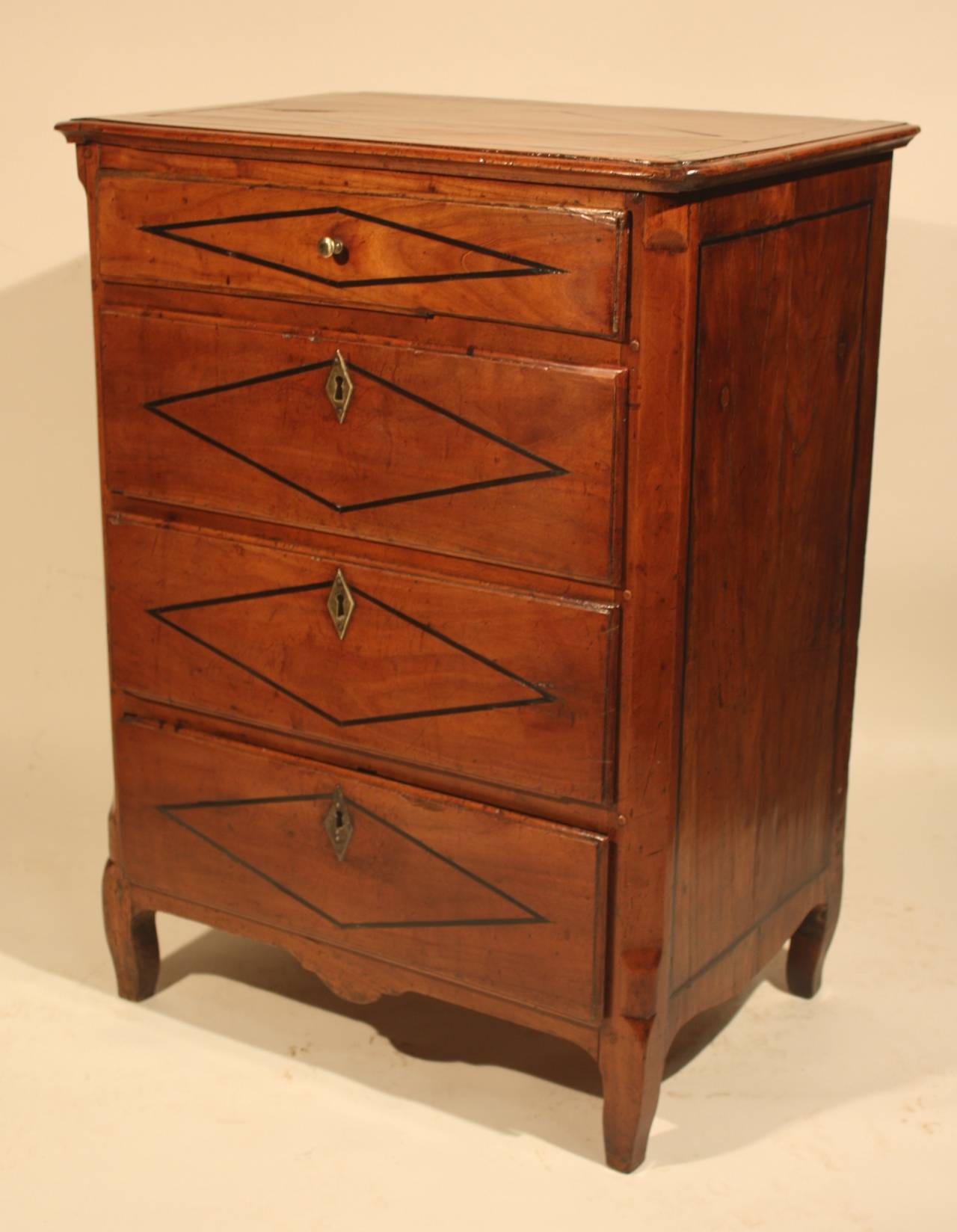 A charming petite commode the perfect size for a bedside stand from the Directoire period circa 1800, in fruitwood with inlaid ebonized diamond patterns on the drawer fronts and top. The piece retains its original hardware and lock with key.