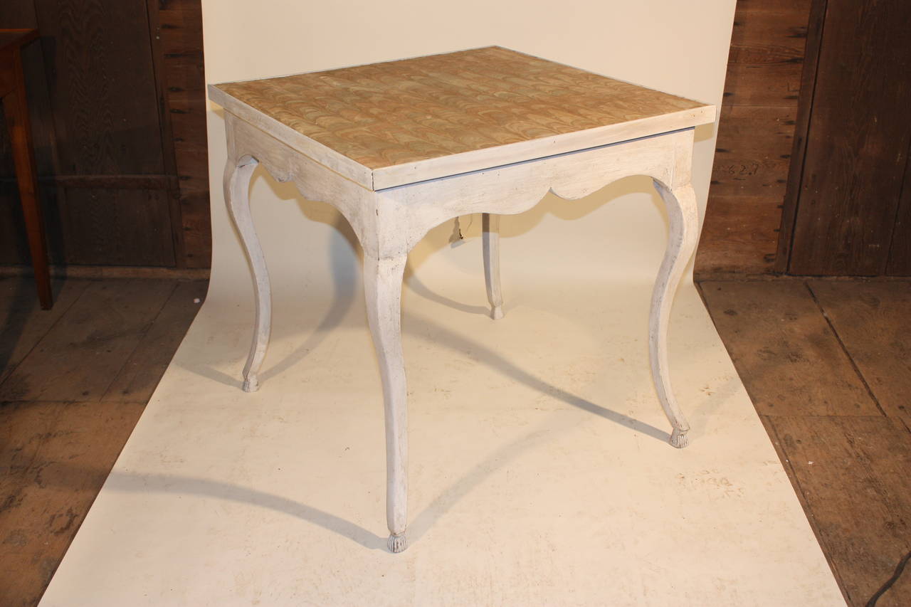 A French Louis XV period, card table circa 1770, in cream painted finish, with cabriolle legs terminating in tassel feet, and a scalloped apron. The top is upholstered in an antique marbleized felt.