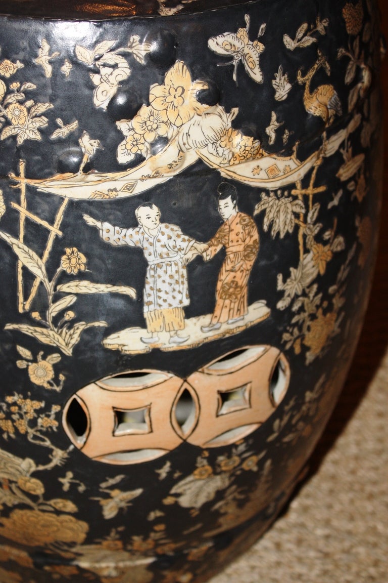 A Chinese ceramic barrel-form garden stool, circa 1920, decorated with chinoiserie figures and flowers in pale salmon and cream-colored glaze with a black background.