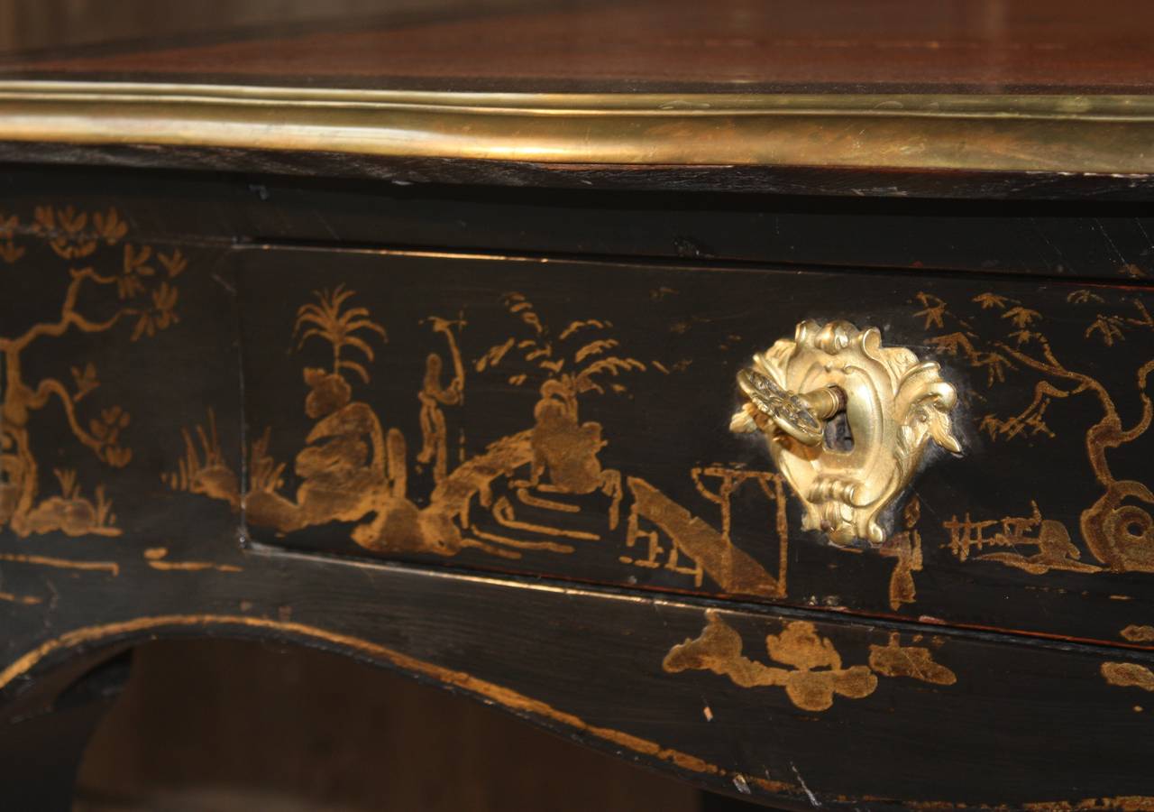 A wonderful Louis XV style bureau plat in ebonized and japanned wood with chinoiserie decoration, circa 1810, with ormolu mounts and gilt bronze trim and sabots, an inset salmon-colored tooled leather writing surface showing the Napoleonic 