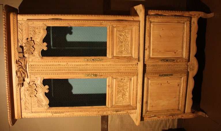 A transitional Louis XV/XVI buffet a deux corps in pine from the Normandy region of France, nicely carved with flowers, love-birds, garlands etc.  The upper doors have wire grills and the interior is painted light blue.  The piece retains its