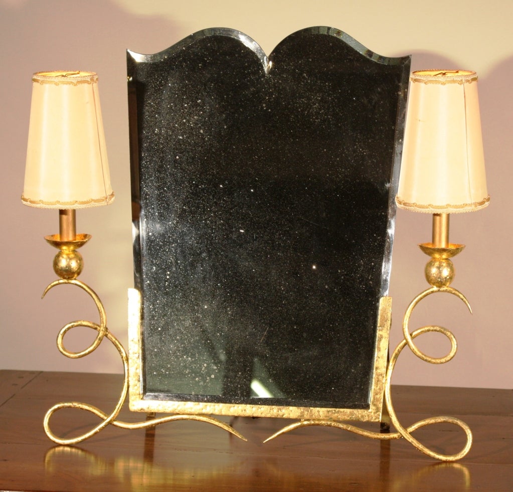 An impressive Art Deco table-top dressing mirror, circa 1925, in hand-wrought gilt iron, with a nicely cut and bevelled inset mirror and two side lights with period shades.