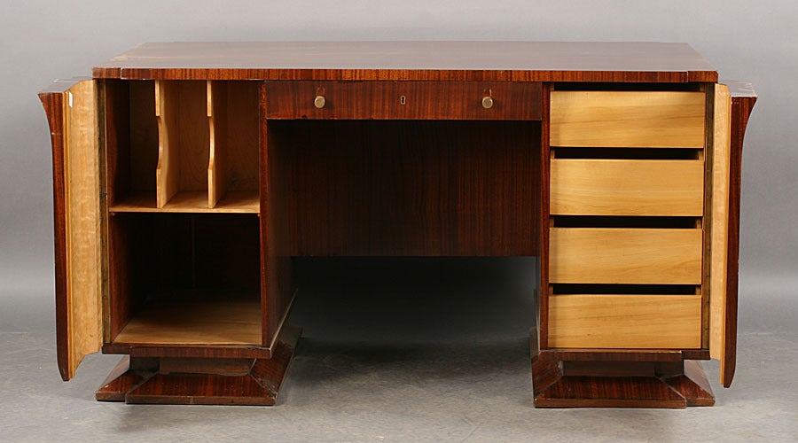 A stylish Art Deco mahogany kneehole desk, French, circa 1930, with double bank of cabinets concealing satinwood drawers and other file compartments, the reverse having a built-in bookshelf.