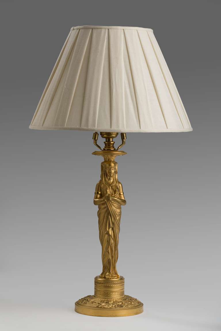The bobeches on an Egyptian draped female figure in a nemes headdress raised on a cylindrical chased socle and spreading circular chased base. Mounted as a lamp.
Measures: 12 in. high candlestick only 21 in overall.