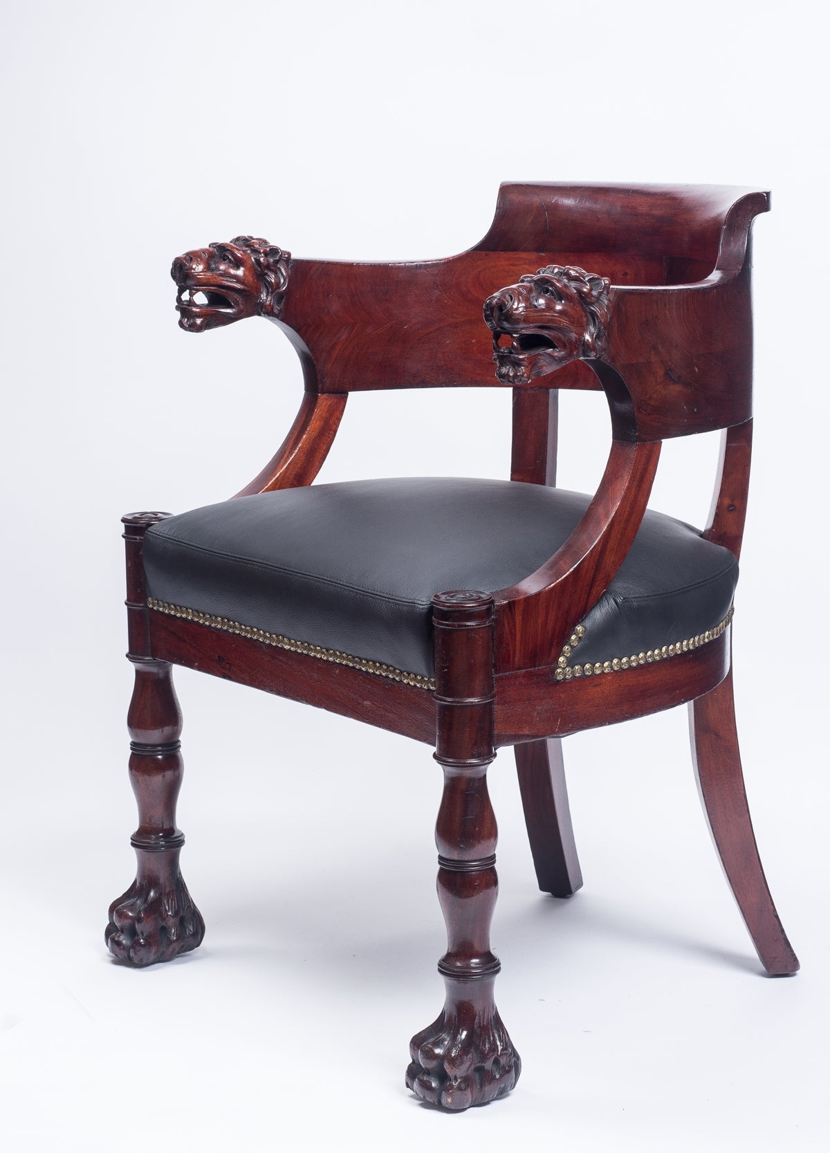The curved back terminating in carved lion's heads above a black leather seat on ring-turned front legs ending in lion feet and back saber legs.