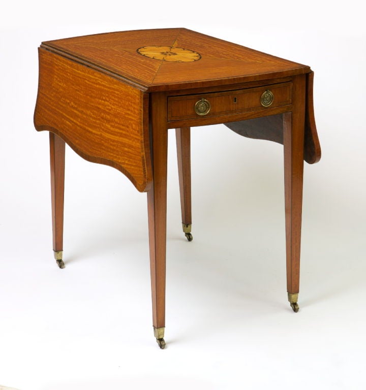 Crossbanded throughout with rosewood‚ with a central sycamore patera to the top and drops of serpentine outline‚ above a frieze drawer to each end‚ raised above tapering legs ending in casters.