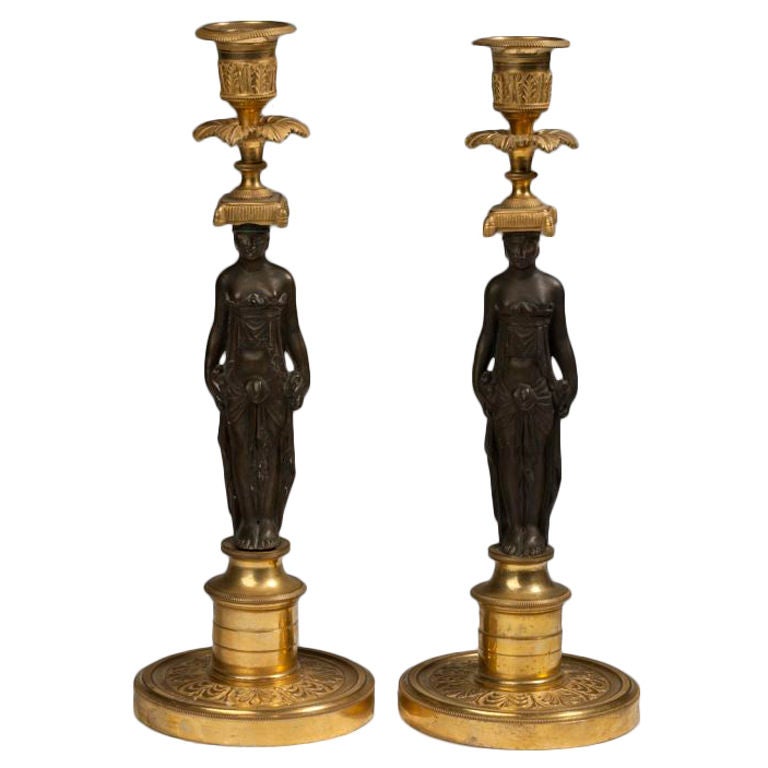 Jeweils eine klassisch drapierte weibliche Figur aus patinierter Bronze, die eine akanthusgegossene Tülle über einer blattförmigen Tropfschale und einem mit Quasten besetzten Kissen trägt, erhöht auf einem mit Palmetten besetzten Rundsockel.