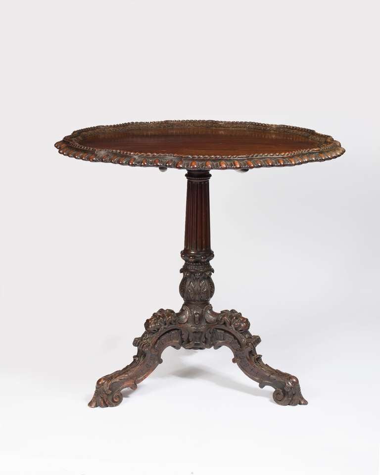 The circular tilt-top with serpentine edge on a fluted and acanthus-clasped baluster column and cabriole legs heavily carved with acanthus leaves, c-scrolls and lion masks, on lion-paw feet.

This splendid tea-table is inspired by the mid-l8th