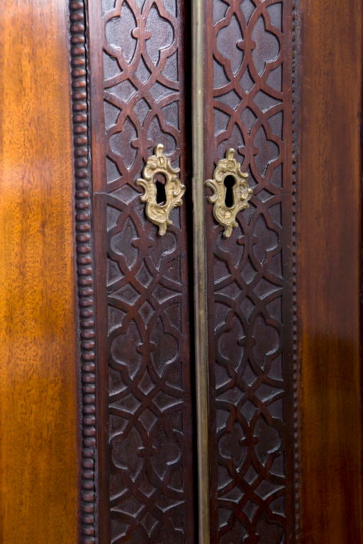 The carved and pierced fretwork cornice above a pair of paneled doors with blind fretwork framing, the interior fitted for shelves and hanging (with one shelf), above two short drawers and two long drawers, raised on blind fretwork carved bracket