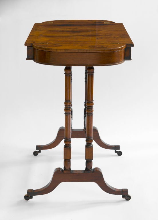 The shaped rectangular top fitted with hinged side compartment‚ above a reeded frieze drawing and a leather inset slide‚ raised on turned columnar supports joined by two baluster-turned stretchers‚ on splayed legs ending in casters.